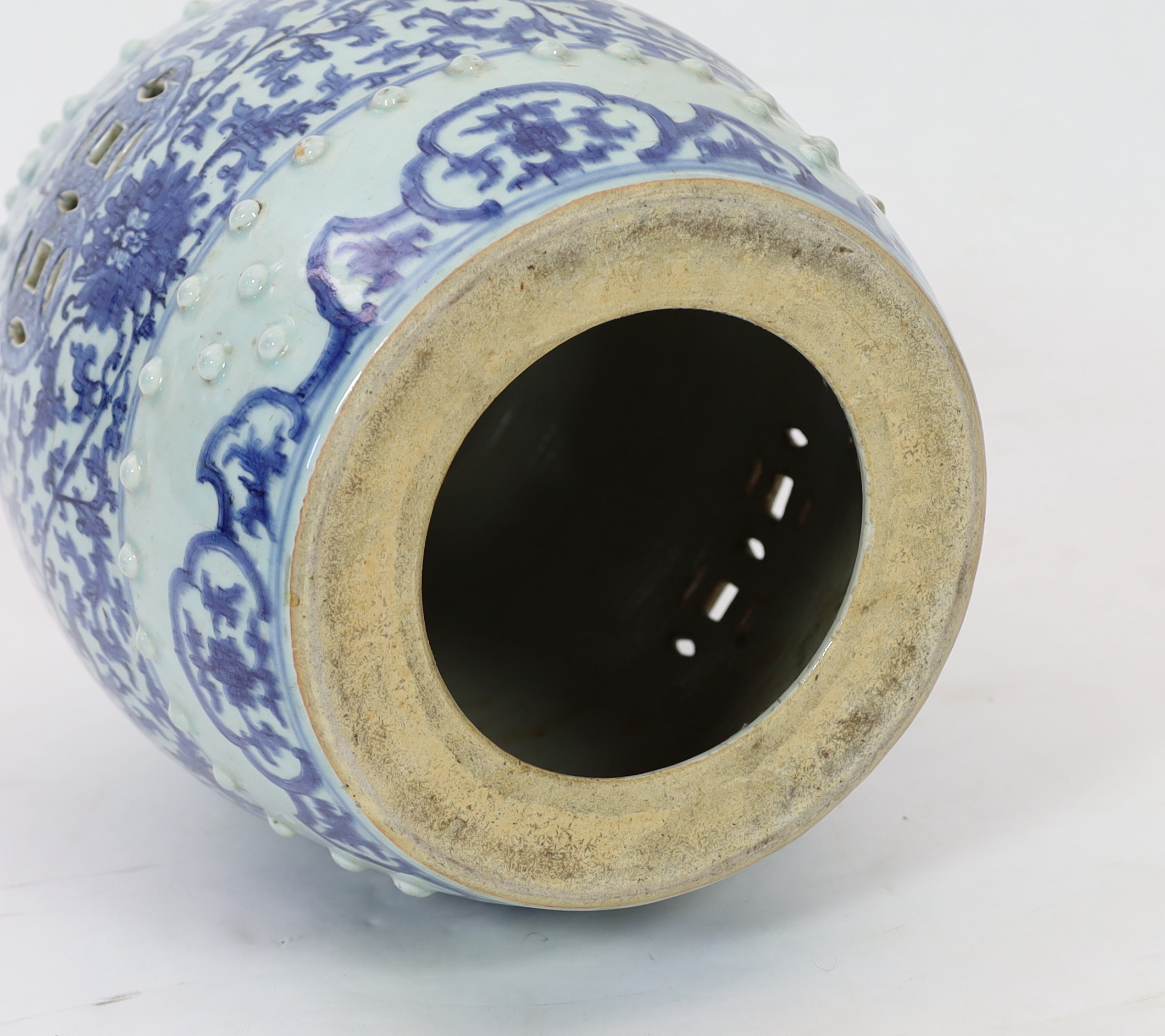 A Chinese blue and white porcelain stool, 19th century, painted with lotus flowers and scrolling foliage, pierced with coin motifs, between bands of raised bosses and foliate lappets, 48cm high